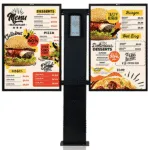 Avio Hybrid intercom post with a central speaker/camera unit flanked by two digital menu boards showing burger, pizza, and dessert options.