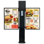 Avio intercom post with built-in camera and keypad flanked by two digital menu boards showing burger, pizza, and dessert options.