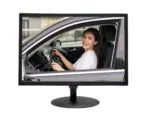 Computer monitor on a stand displaying a live video feed of a smiling woman driving her car, used for drive-thru order-taking.