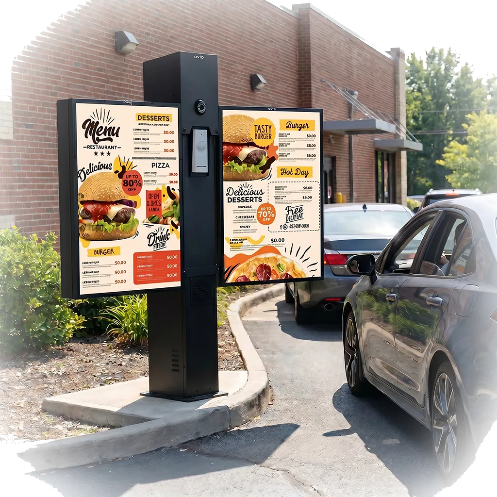 Outdoor drive-thru menu board post with two digital menu screens showing burger, pizza, and dessert options, installed at a restaurant with cars in the drive-thru lane.